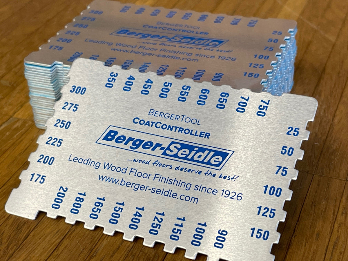 Ein Stapel silberner Metallkarten mit der Aufschrift "Berger-Seidle CoatController" und Messkerben an den Rändern, die für die Bearbeitung von Holzböden verwendet werden, liegt auf einer Holzfläche.